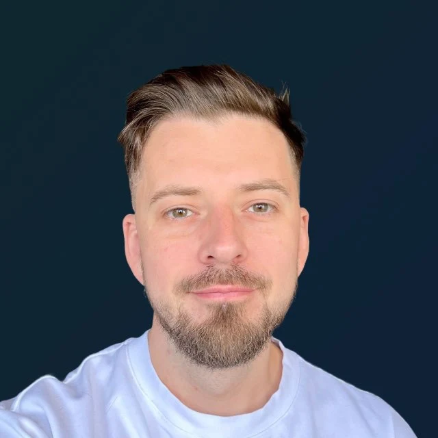Portrait of Oliver Ustinovich, smiling, in a white T-shirt against a dark blue background.